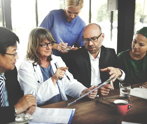 2 female doctors, two men and one woman sitting at a table taking notes and looking at an ipad