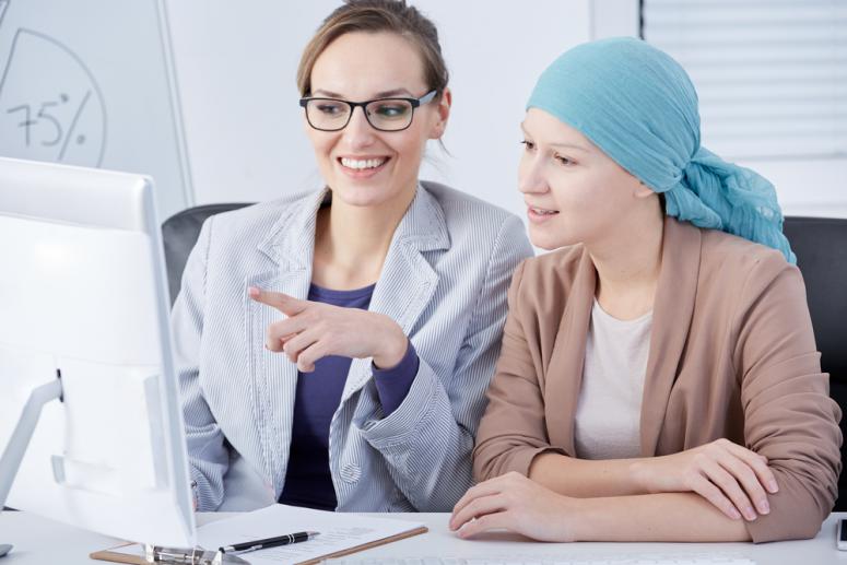 Female cancer patient working at office, talking with workmate